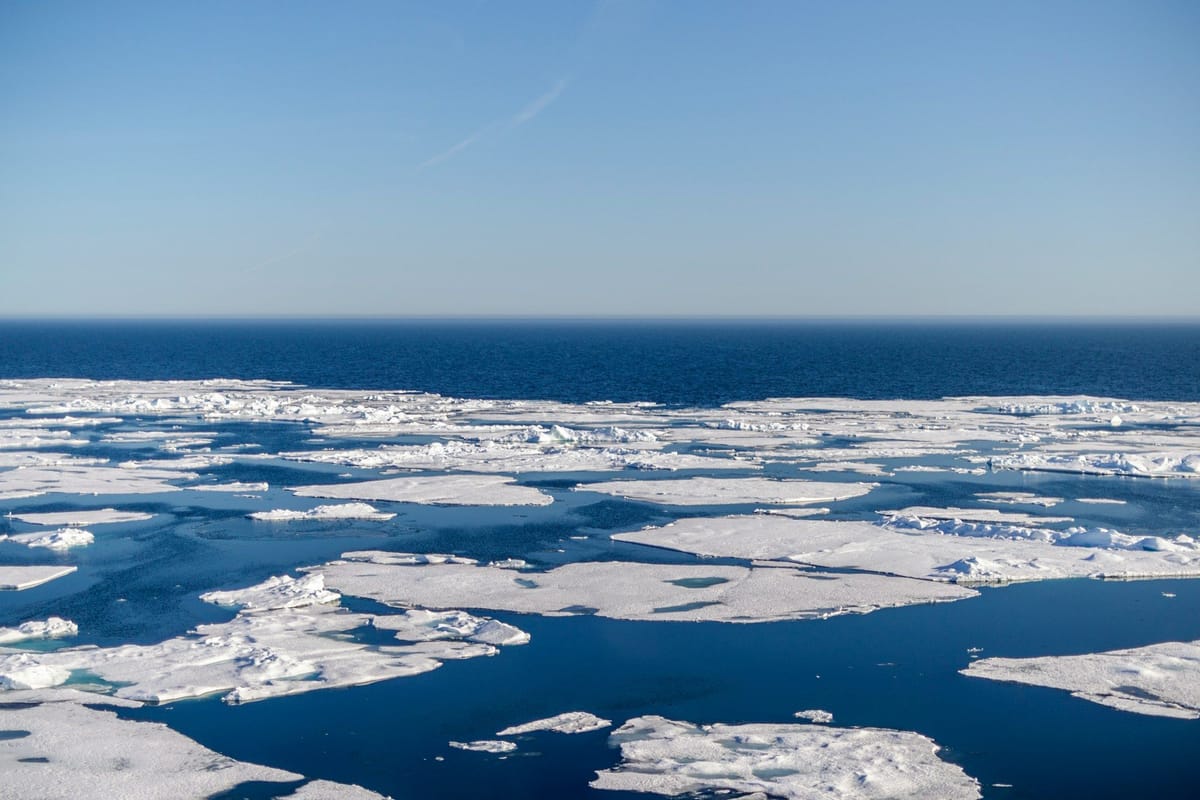 Broken sea ice floating across deep blue Arctic waters beneath a clear sky.