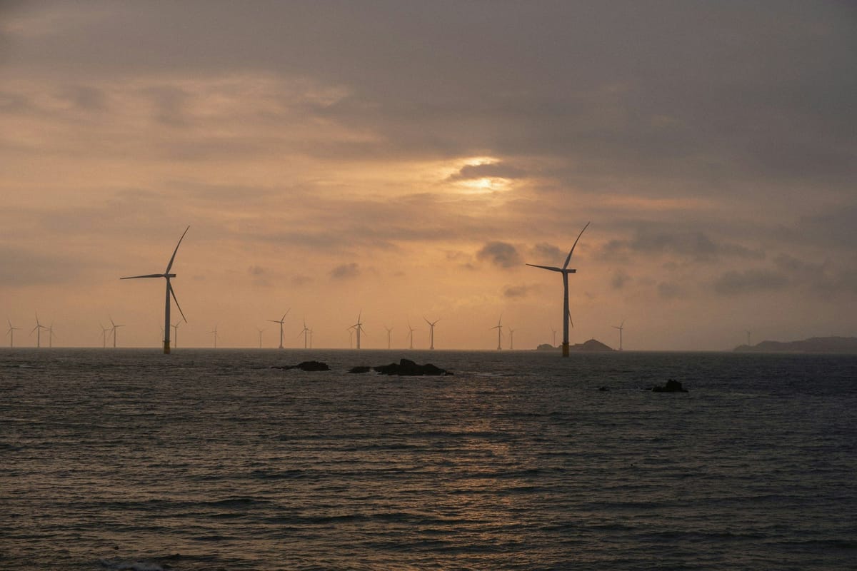 Offshore wind turbines stretching across the ocean beneath a warm, clouded sunset sky.