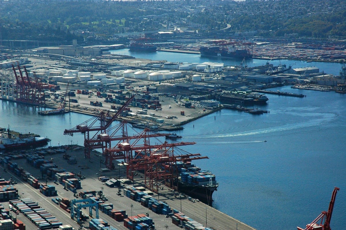 Aerial view of a large industrial port with container terminals, storage tanks, cargo ships, and cranes surrounding the harbour.