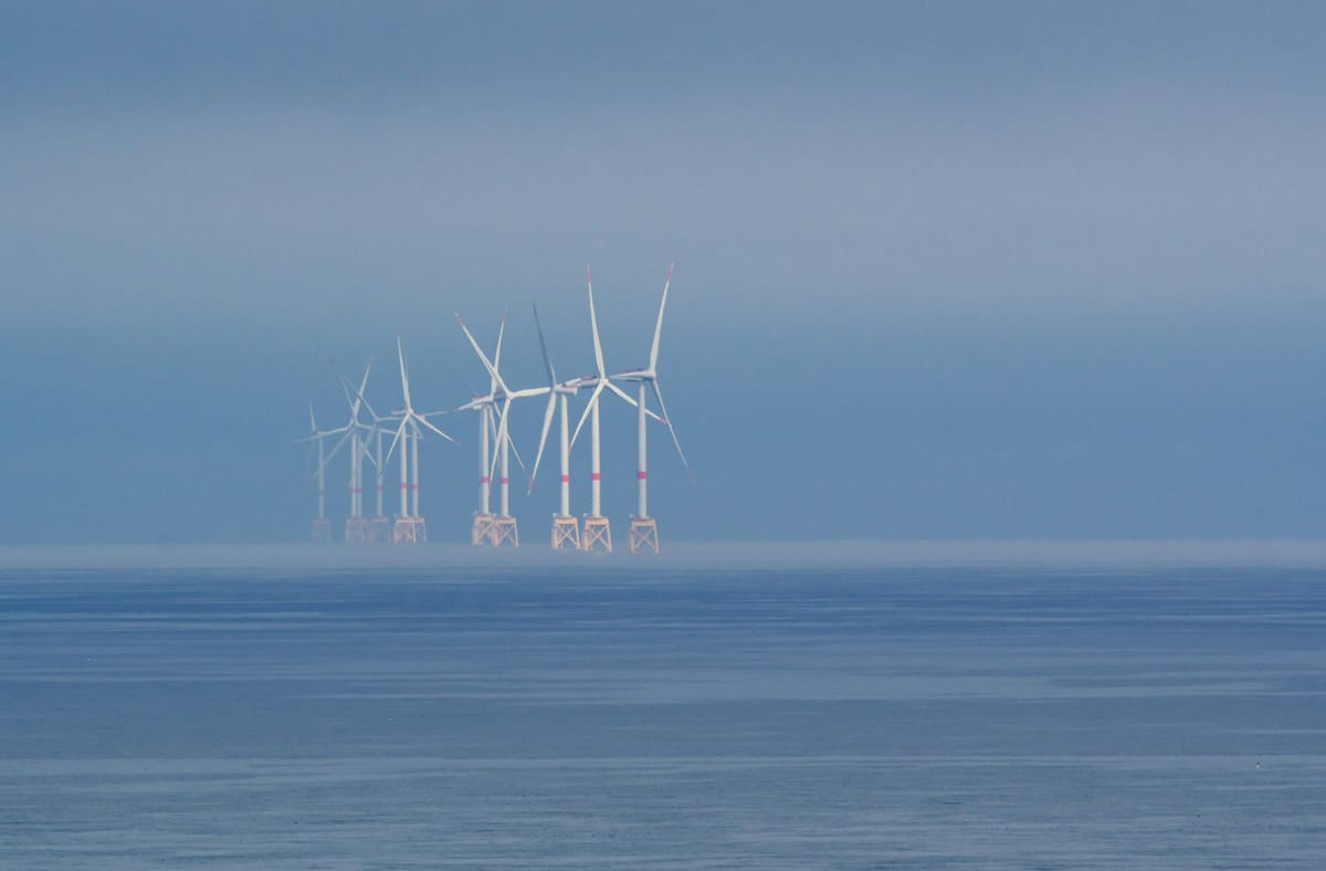Offshore wind turbines fading into mist over calm ocean waters.
