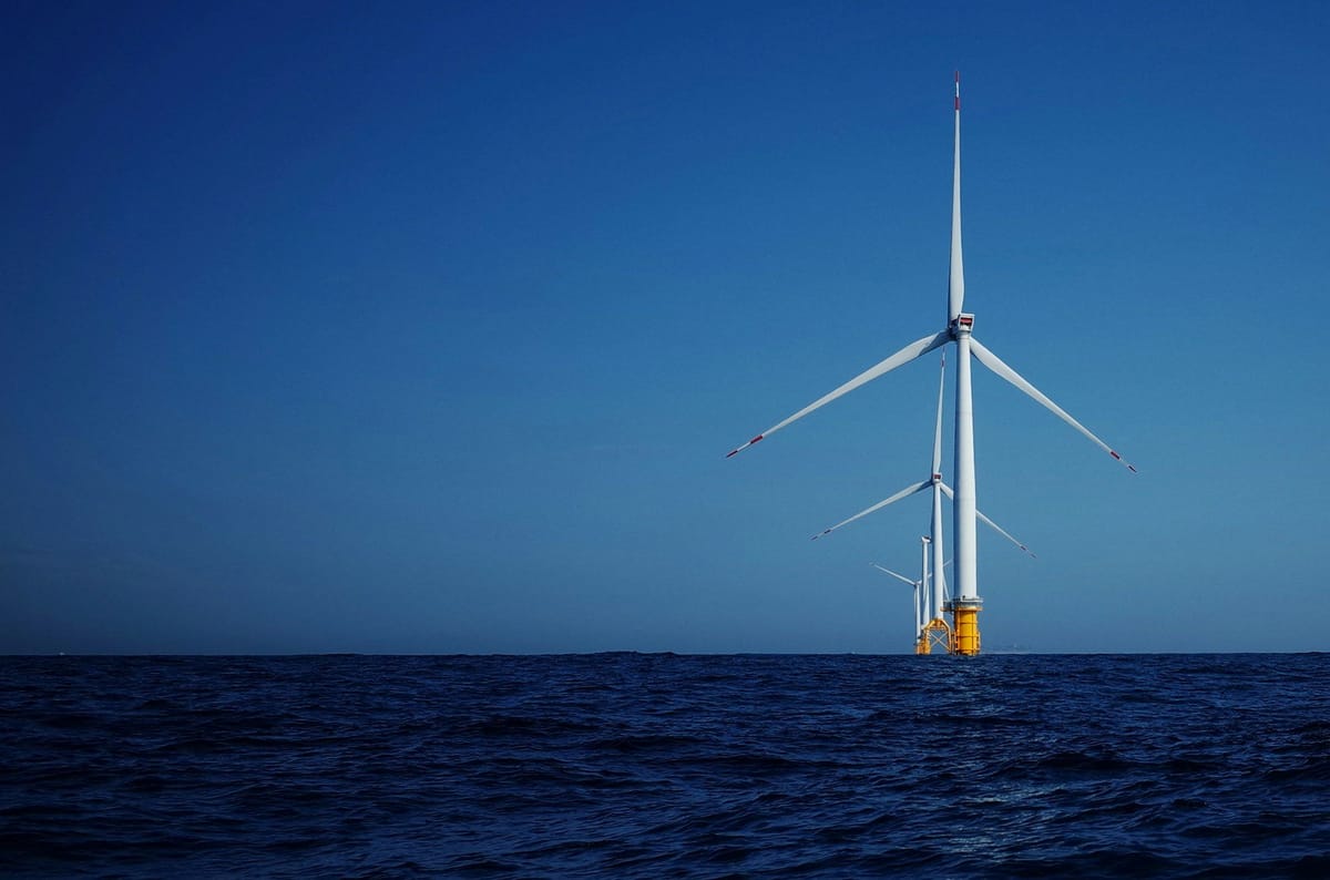 Offshore wind turbines rising from the ocean beneath a clear blue sky.