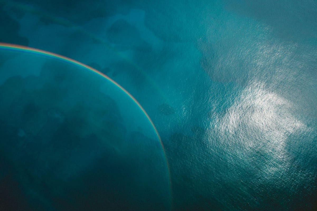 A rainbow arcing over deep blue ocean water, with sunlight reflecting on the surface.