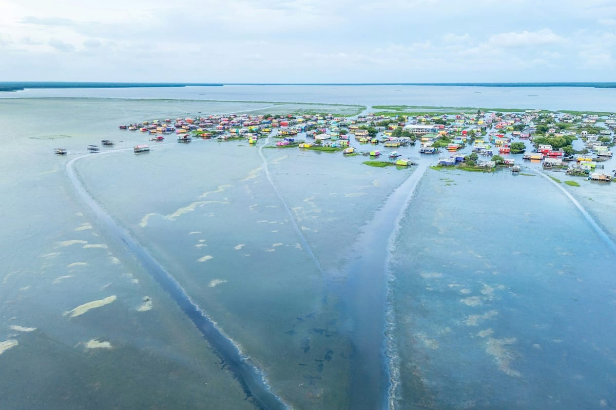 Aerial view of a low-lying coastal community with colourful homes surrounded by shallow water and wetlands.