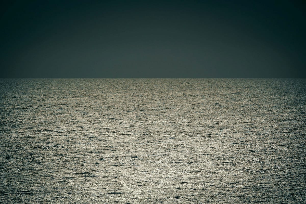 Sunlight shimmering across the open ocean beneath a dark, cloudless sky.