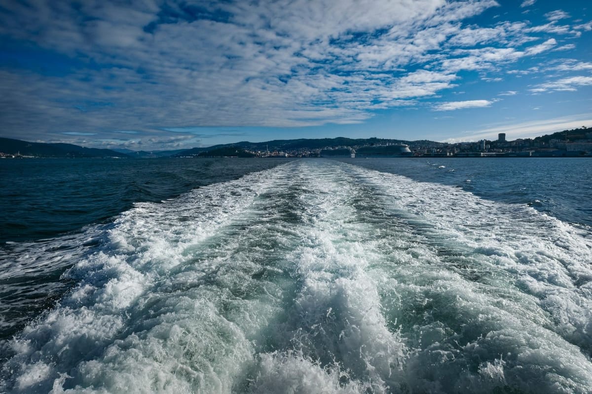 A boat’s white wake stretching across dark blue ocean water toward the horizon.