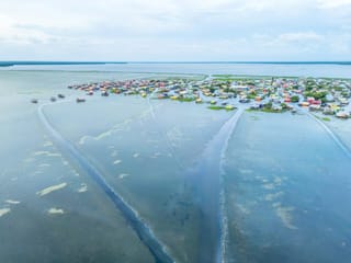 Aerial view of a low-lying coastal community with colourful homes surrounded by shallow water and wetlands.