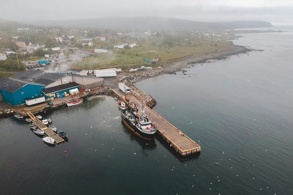 Aerial view of a small coastal fishing community in fog, working dock with vessels moored, overcast grey sky, Atlantic Canada.