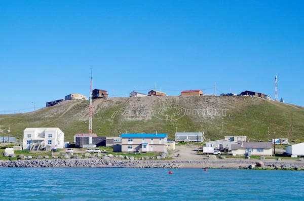 Coastal community of Pond Inlet, Nunavut, with homes along the shoreline and “Pond Inlet” spelled across the hillside.