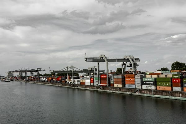 Shipping containers and cargo cranes lining a busy port terminal beside the water.
