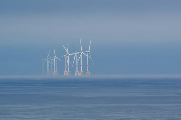 Offshore wind turbines fading into mist over calm ocean waters.