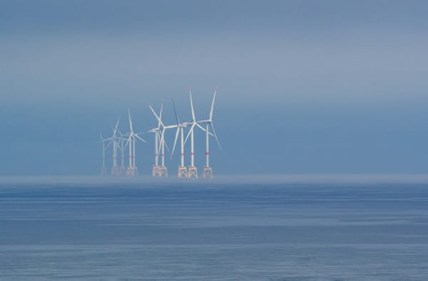 Offshore wind turbines fading into mist over calm ocean waters.