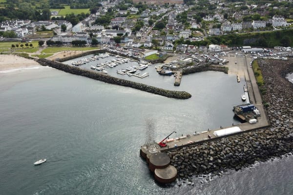Aerial view of a coastal harbour protected by long rock breakwaters, with a marina and town along the shoreline.