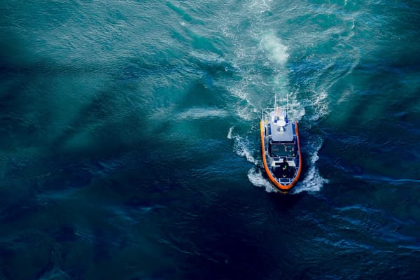 Aerial view of a small patrol boat cutting through deep blue ocean water, leaving a foamy wake.