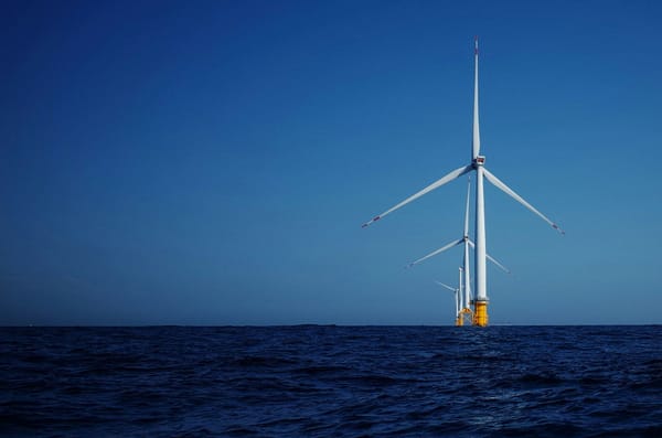 Offshore wind turbines rising from the ocean beneath a clear blue sky.
