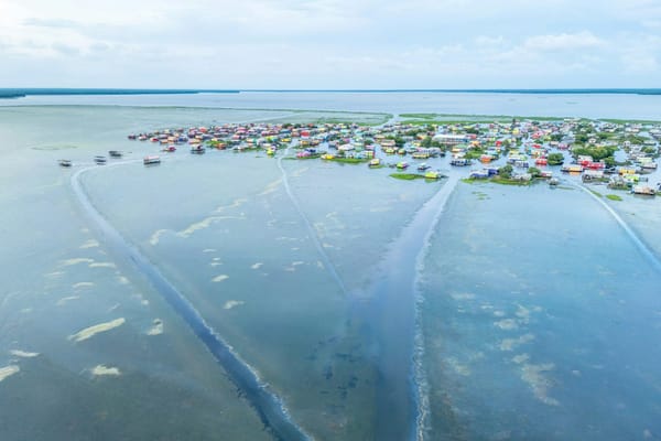 Aerial view of a low-lying coastal community with colourful homes surrounded by shallow water and wetlands.