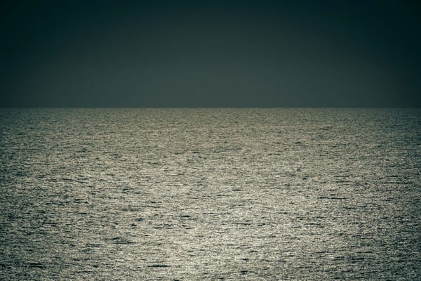 Sunlight shimmering across the open ocean beneath a dark, cloudless sky.