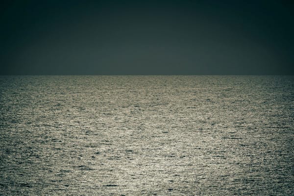 Sunlight shimmering across the open ocean beneath a dark, cloudless sky.