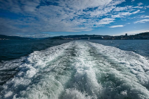 A boat’s white wake stretching across dark blue ocean water toward the horizon.