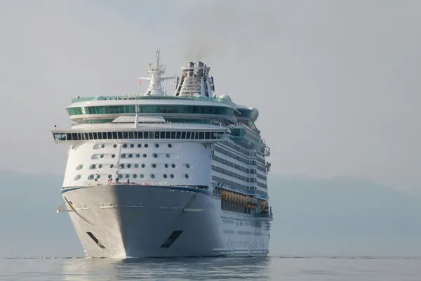 Large cruise ship travelling through calm coastal waters beneath a hazy sky.