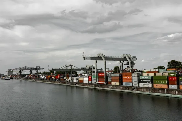 Shipping containers and cargo cranes lining a busy port terminal beside the water.