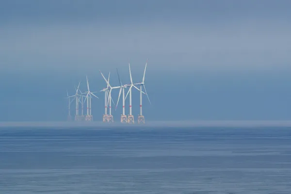 Offshore wind turbines fading into mist over calm ocean waters.