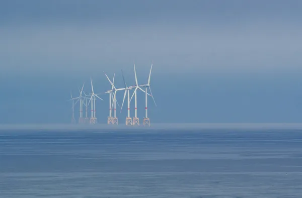 Offshore wind turbines fading into mist over calm ocean waters.
