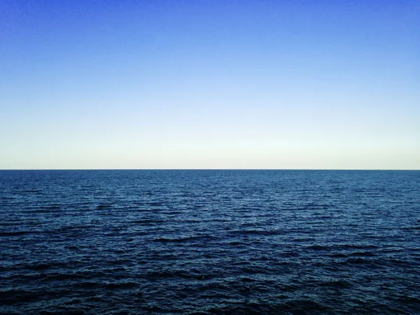 Open ocean stretching to the horizon beneath a clear blue sky.