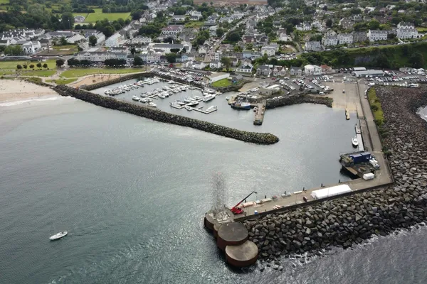 Aerial view of a coastal harbour protected by long rock breakwaters, with a marina and town along the shoreline.