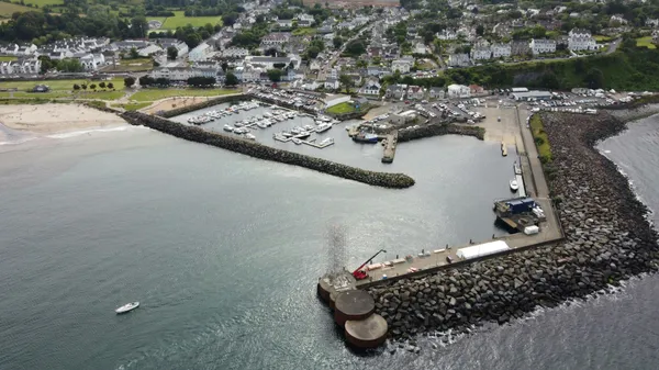 Aerial view of a coastal harbour protected by long rock breakwaters, with a marina and town along the shoreline.