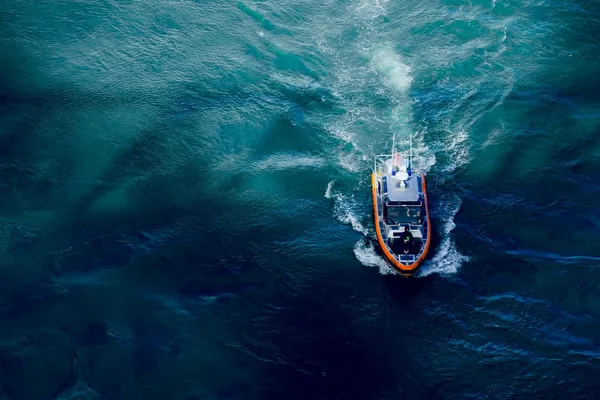 Aerial view of a small patrol boat cutting through deep blue ocean water, leaving a foamy wake.