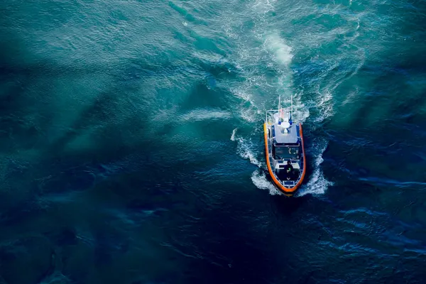 Aerial view of a small patrol boat cutting through deep blue ocean water, leaving a foamy wake.