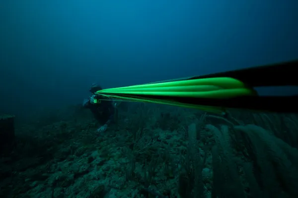 Scuba diver swimming above a coral reef, with bright green fins extending toward the camera.