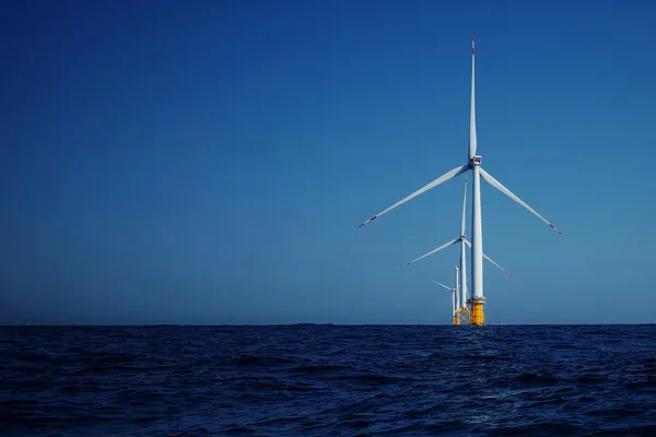Offshore wind turbines rising from the ocean beneath a clear blue sky.
