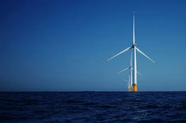 Offshore wind turbines rising from the ocean beneath a clear blue sky.