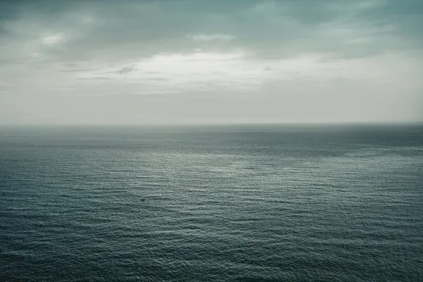 Grey open ocean stretching to the horizon beneath an overcast sky.
