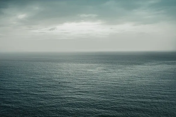 Grey open ocean stretching to the horizon beneath an overcast sky.