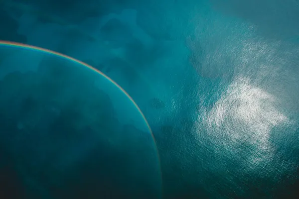A rainbow arcing over deep blue ocean water, with sunlight reflecting on the surface.