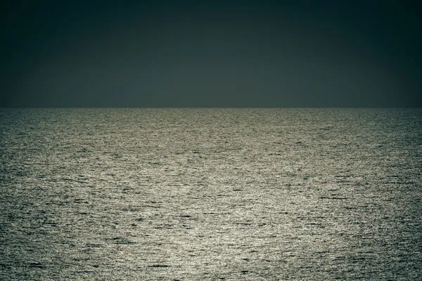 Sunlight shimmering across the open ocean beneath a dark, cloudless sky.