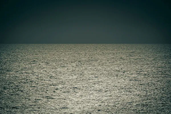 Sunlight shimmering across the open ocean beneath a dark, cloudless sky.
